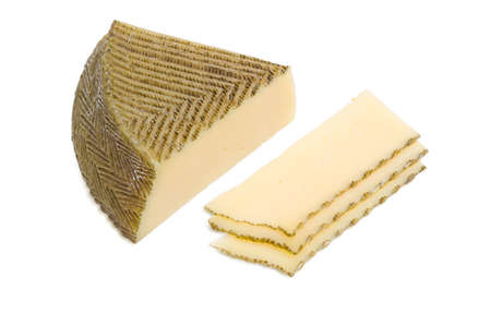 Piece and several slices of semi-hard Spanish cheese with dark coating manufactured from mixtures of cow and sheep milk on a light backgroundの写真素材