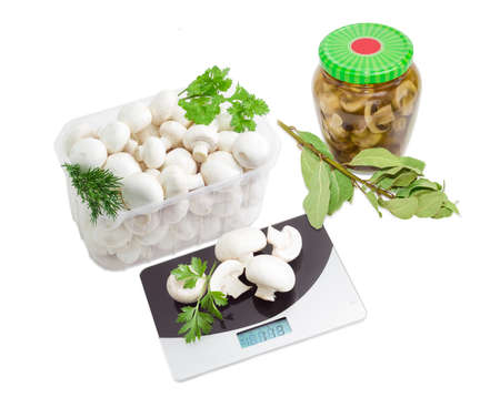 Fresh button mushrooms in a transparent plastic tray, canned mushrooms in glass jar, digital kitchen scale, branches of a dried bay leaf, fresh branches of coriander, dill and parsley on a light backgroundの写真素材
