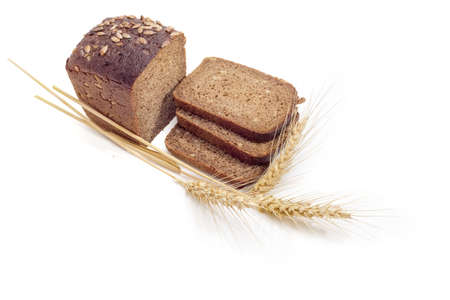 Partly sliced brown bread with whole grain of a sunflowers and three wheat spikes on a light backgroundの写真素材