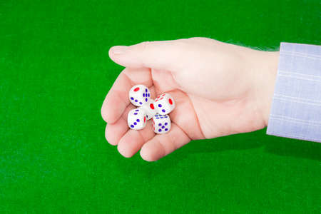 Traditional plastic white six-sided dice with red and blue dots in male hand over a table covered green cloth.の写真素材