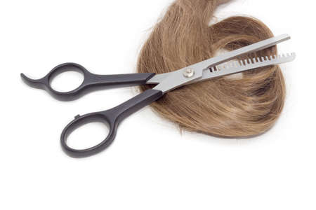 Specialized type of hairdressers scissors - thinning shears  against the backdrop of strand of female hair on a light background.の写真素材