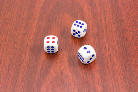 Three traditional plastic white six-sided dice with red and blue dots and rounded corners on wooden surfaceの写真素材