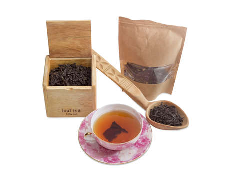 Saucer and cup of black tea, different varieties of tea leaves in paper bag, wooden box and wooden spoon on a light backgroundの写真素材