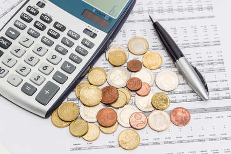 Several euro coins from 1 cents to 2 euro scattered on the printed table with data, pen and fragment of a calculatorの写真素材