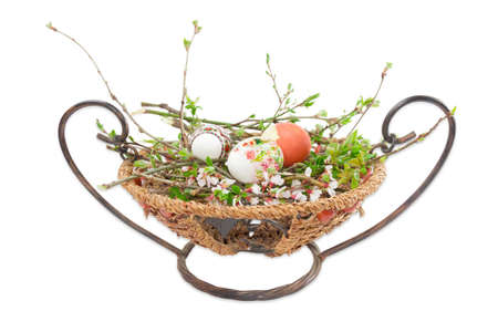 Several Easter eggs with a different patterns, decorating and drawings on branches with blooming leaves and flowers in a wicker basket on a light backgroundの写真素材