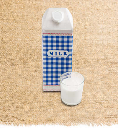 Plastic coated paper carton with pasteurized cows milk and a glass of milk on a surface covered sackclothの写真素材