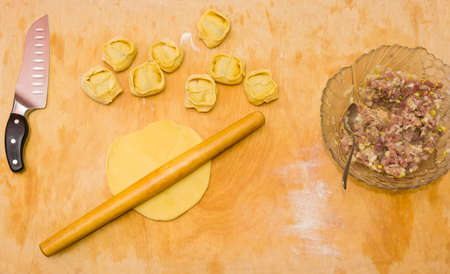 Uncooked manti, ingredients and kitchenware on a wooden cutting board during cooking dumplingsの写真素材