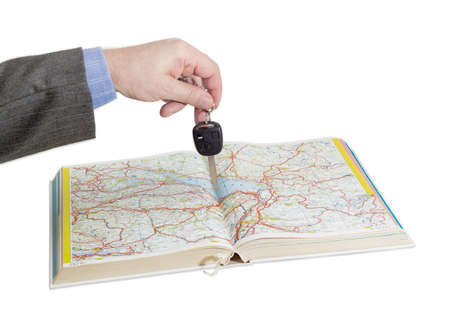 Male hand with car keys over an open old road atlas on a light backgroundの写真素材