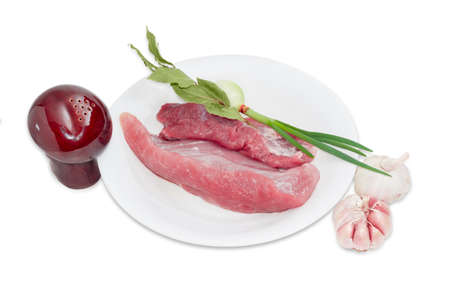 Several pieces of a fresh uncooked pork, branch of dried bay leaves, green onion on white plateの写真素材