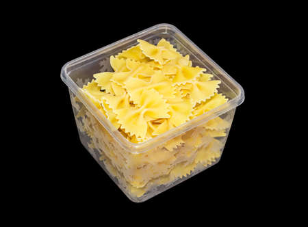 Uncooked bow-tie pasta in transparent plastic tray on a dark backgroundの写真素材