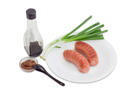 Two fried thick frankfurters and green onion on a white dish, coarse French mustard and soy sauce on a light backgroundの写真素材