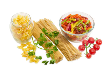 Uncooked dried long pasta two varieties, colored spiral pasta and farfalle pasta, sprigs of parsley and cluster of cherry tomatoes on a light backgroundの写真素材