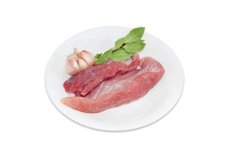 Several pieces of a fresh uncooked pork, branch of dried bay leaves and garlic on white plate on a light backgroundの写真素材