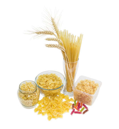 Uncooked dried long pasta and wheat spikes in glass, other pasta different varieties, shapes and colors on a light backgroundの写真素材