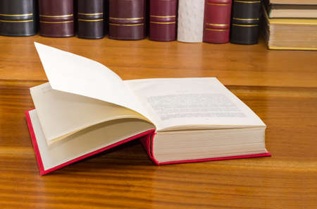 Open book with red cover on a wooden table against of the other books on the backgroundの写真素材