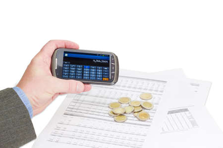 Male hand with smartphone in calculator mode against several euro coins on data tables on a light backgroundの写真素材