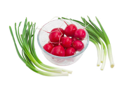 Fresh washed red radish in transparent glass bowl against the two bunches of green onion on a light backgroundの写真素材