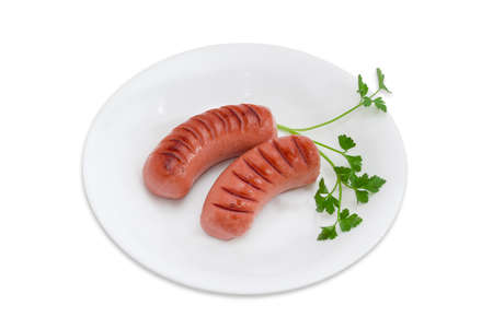 Two fried thick frankfurters and sprig of parsley on a white dish on a light backgroundの写真素材