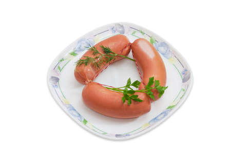 Bundle of three uncooked thick frankfurters and sprigs of dill and parsley on a dish on a light backgroundの写真素材