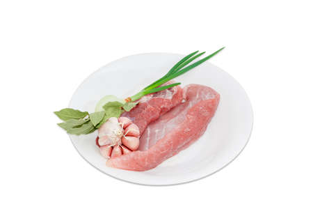 Several pieces of a fresh uncooked pork, branch of dried bay leaves, green onion and garlic on white plate on a light backgroundの写真素材