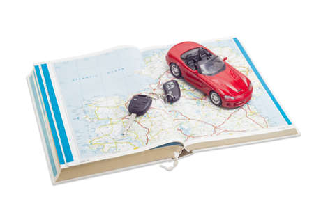 Red toy car cabriolet and car keys on the old open road atlasの写真素材