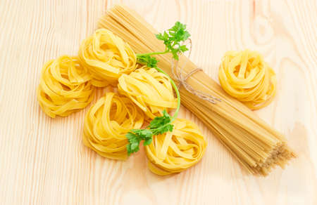Uncooked dried egg pasta tagliatelle, bundle of long pasta and sprig of parsley on a light wooden surfaceの写真素材
