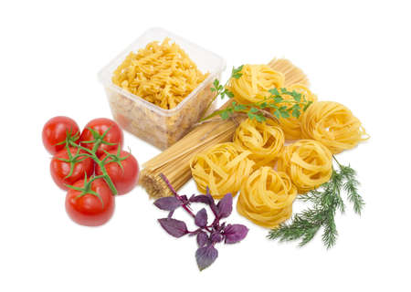 Uncooked dried long pasta, tagliatelle egg pasta, plastic tray with spiral pasta, bunch of tomatoes and sprigs of basil, dill and parsley on a light backgroundの写真素材