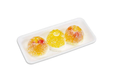 Three yellow fruit jelly candies gelatin based with jam inside and coated in granulated sugar in a small plastic tray on a light backgroundの写真素材