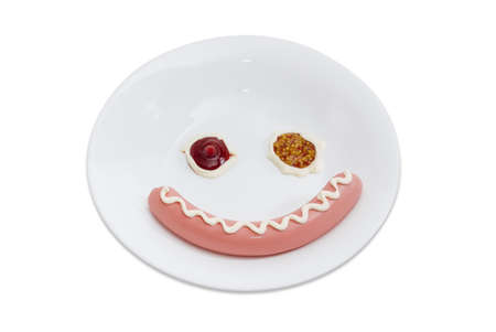 Boiled sausage and condiments laid out on a white dish in the form of smiling face on a light backgroundの写真素材