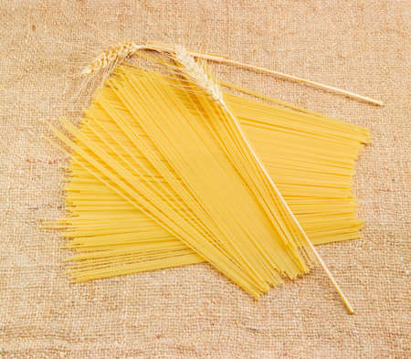Uncooked dried long pasta and two wheat spikes on a sackclothの写真素材