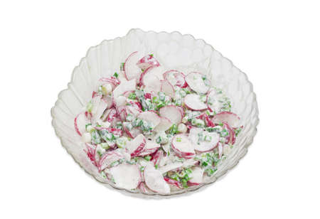 Top view to a salad of fresh sliced red radish, green onion with sour cream in transparent glass salad bowl on a light backgroundの写真素材