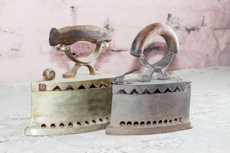 Two old charcoal irons on table with old tablecloth against the background of the brickworkの写真素材