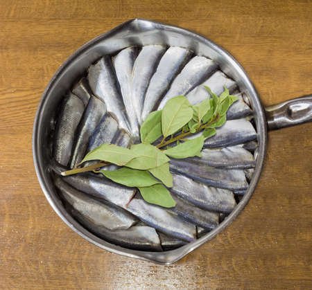Cut and prepared for cooking raw baltic herring and a sprig of bay leaf in a stainless steel pan on a wooden tableの写真素材