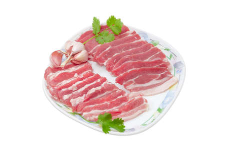 Several slices of uncooked streaky pork belly bacon, garlic and sprigs of cilantro on a dish on a light backgroundの写真素材