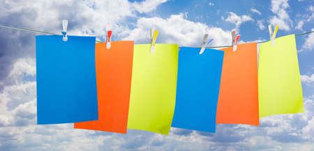 Blank sheets of colored paper, fixed a plastic clothespins with colored inserts on clothesline against the sky with cloudsの写真素材