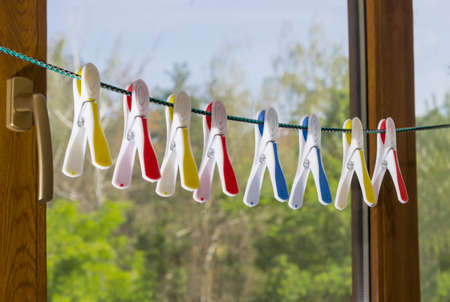 Spring-type plastic clothespins with multi-colored rubber inserts on a clothes line on a blurred background of the window, the sky and the treesの写真素材