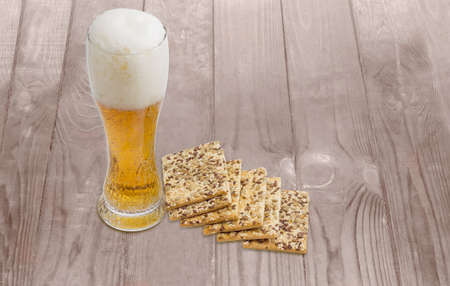 Beer glass with lager beer and savory biscuits with sesame seeds, flax seeds and sunflower on a wooden surfaceの写真素材