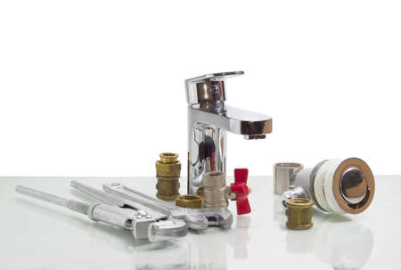 Single handle mixer tap, plumber wrench, adjustable wrench and plumbing components on a reflective...