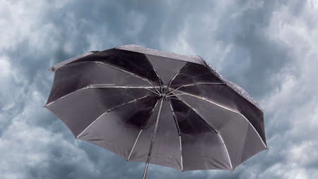 Open male black folding umbrella against the background of sky with thunder cloudsの写真素材