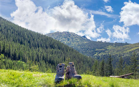 Pair of leather light brown trekking shoes in a clearing in the grass against the backdrop of...