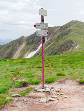 Signpost of hiking trails indicating the direction, distance and time on the background of mountain peak and skyの写真素材