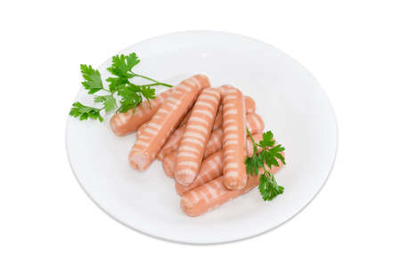 Several uncooked striped frankfurters and sprigs of parsley on a white dish on a light backgroundの写真素材