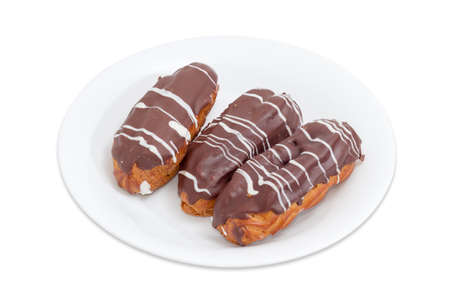 Three eclairs with whipped cream and chocolate icing on a white dish on a light backgroundの写真素材