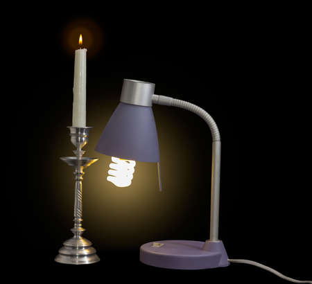Luminous light fixture with compact fluorescent lamp and burning candle in an old metal candlestick on a dark backgroundの写真素材