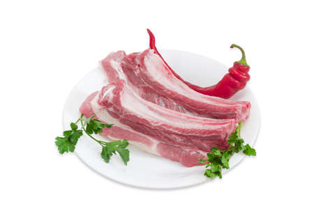 Two pieces of uncooked pork belly with ribs, chili pepper and twigs of parsley and cilantro on a dish on a light backgroundの写真素材