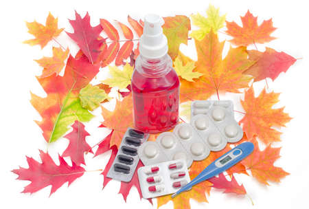 Blue electronic medical thermometer, throat spray, several packaging of medications and autumn leaves on a light backgroundの写真素材