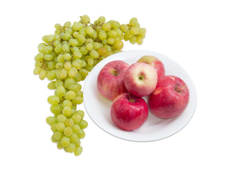 Several red apples on white dish and cluster of white table grapes beside on a light backgroundの写真素材