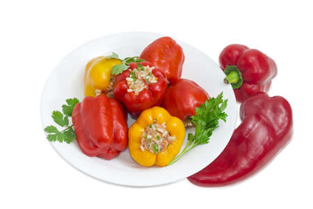 Cooked stuffed red and yellow bell peppers and twigs of greenery on a white dish  and two uncooked red bell peppers separately on a light backgroundの写真素材