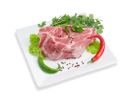 Piece of a fresh uncooked pork neck, green and red chili, black and red pepper, lettuce, parsley and cilantro on a white square dish on a light backgroundの写真素材