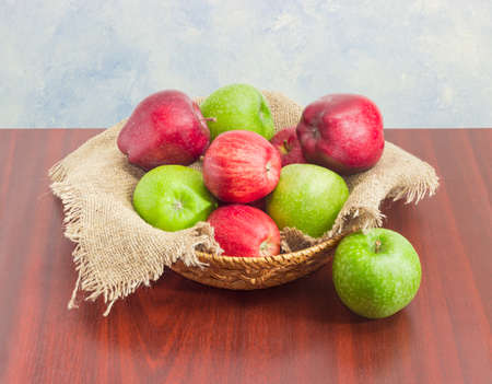 Pile of a red and green apples on a sackcloth in a small wicker basket on a dark wooden surface
の写真素材